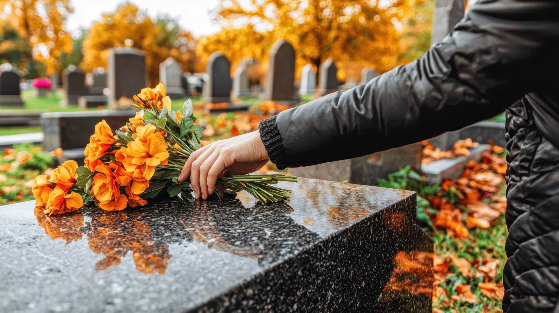 Person Placing Flowers on Cemetery Gravestone in Autumn Season