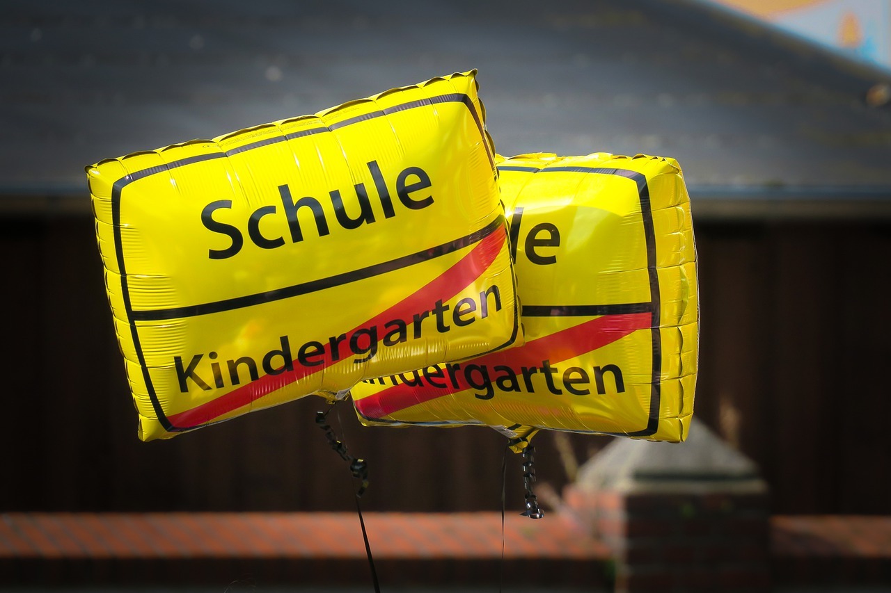 Zwei quadratische Luftballons in Anlehnung an Ortseingangsschilder, die den Abgang vom Kindergarten in die Schule anzeigen