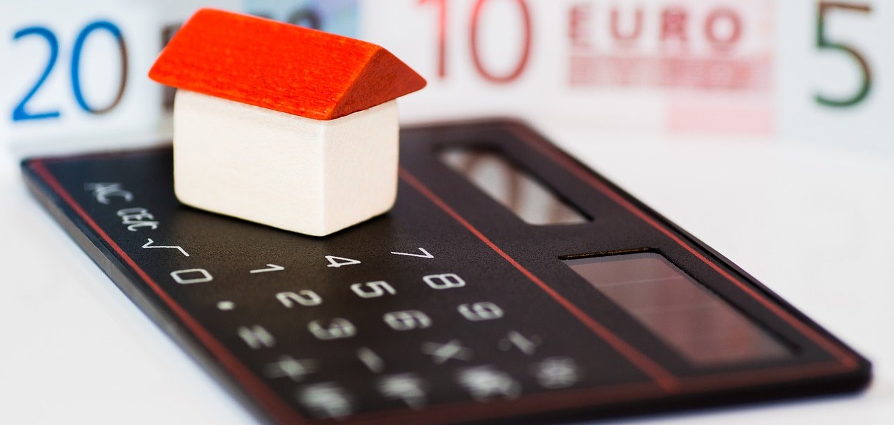 Taschenrechner mit kleinem Spielzeughaus und Eurobanknoten im Hintergrund